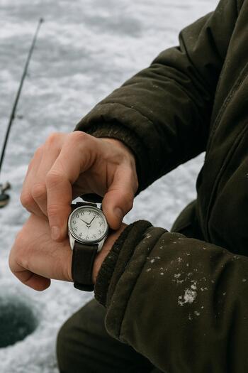 Рыбак смотрит на часы, стоя на маршруте зимней рыбалки